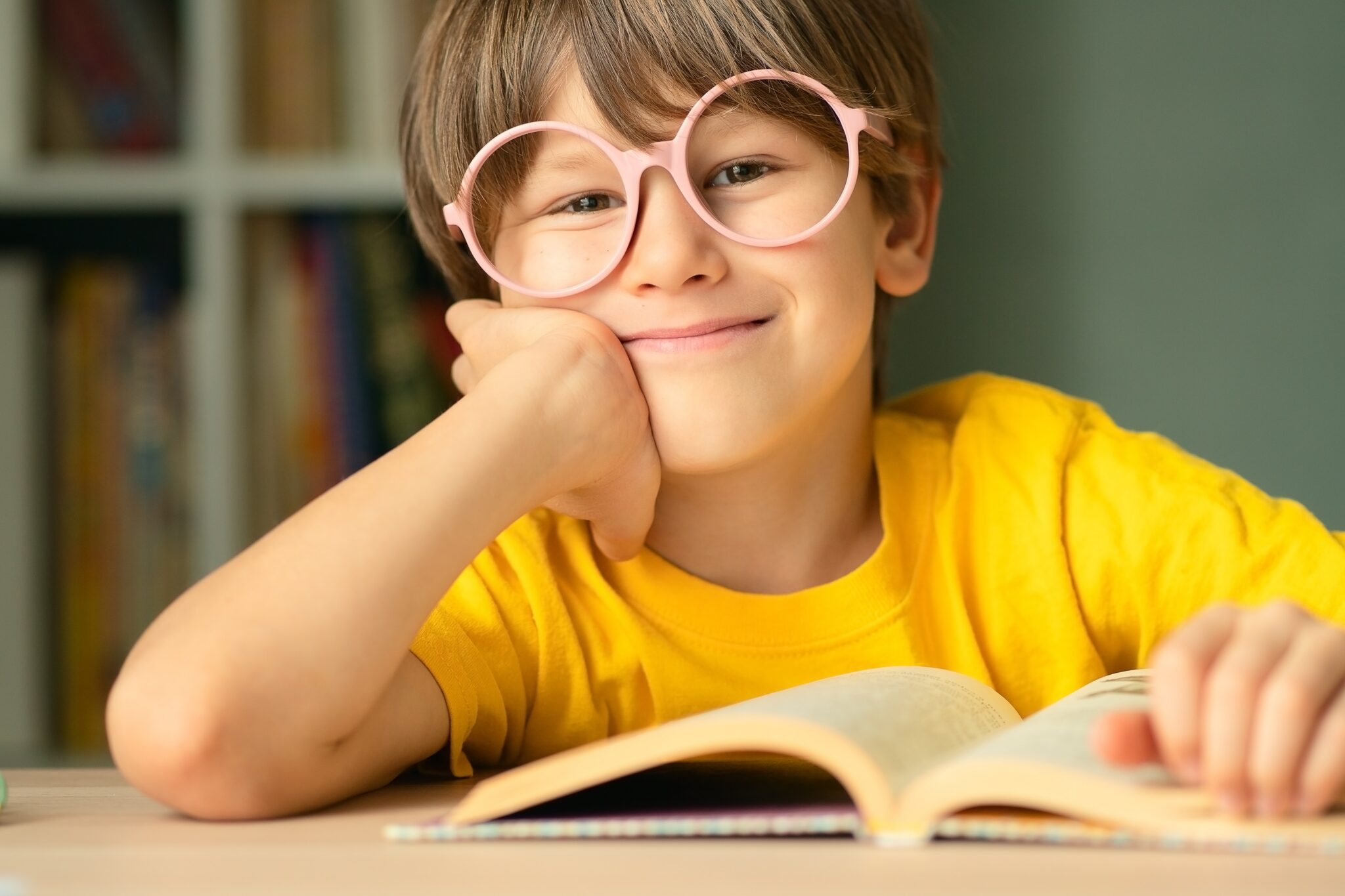 Smiling boy wearing round glasses with impact-resistant polycarbonate lenses reading a book