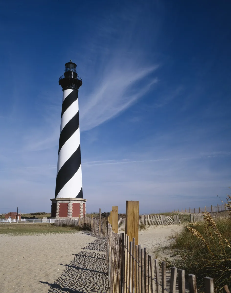 Black and white spiral-striped Cape Hatteras Lighthouse behind a sand fence on the Outer Banks